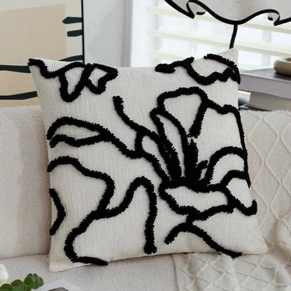 Coussin décoratif aux motifs géométriques noirs sur fond crème, posé sur un canapé moderne