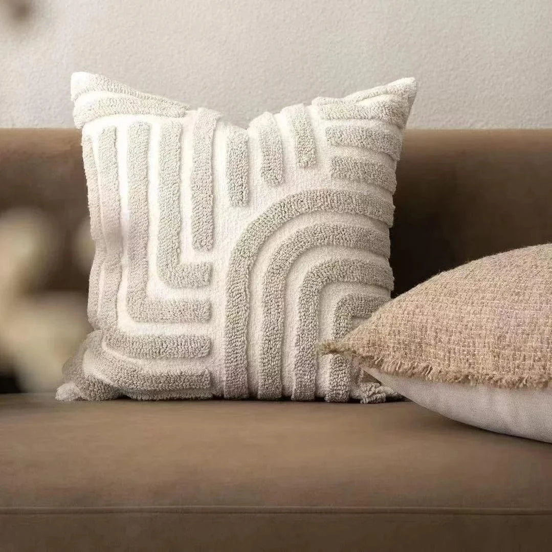 Coussin décoratif en tissu texturé beige avec motifs géométriques, posé sur un canapé moderne