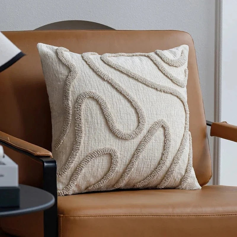 Coussin décoratif beige avec motifs géométriques en relief, posé sur un fauteuil en cuir dans un salon moderne