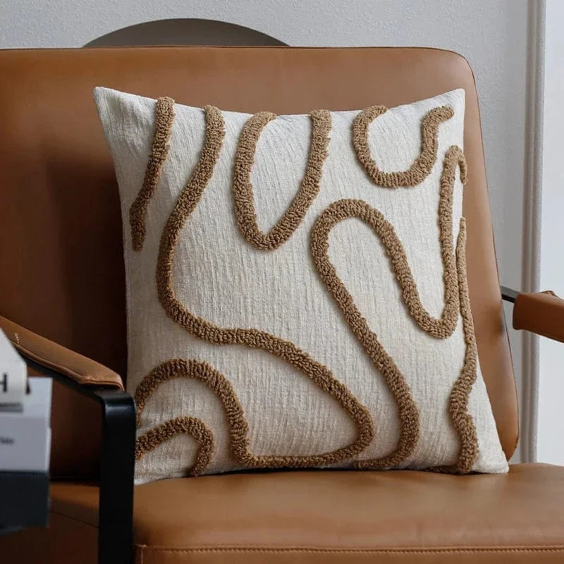 Coussin décoratif aux motifs géométriques en beige et crème, posé sur un fauteuil en cuir dans un salon moderne