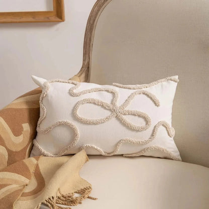 Coussin déco blanc avec motifs en corde beige, posé sur un canapé beige, ajoutant une touche élégante à l'intérieur