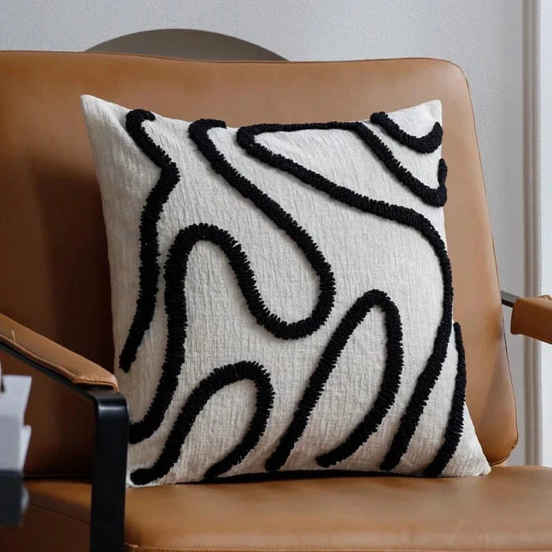 Coussin décoratif avec motifs géométriques noirs sur fond crème, posé sur un fauteuil en cuir dans un salon moderne