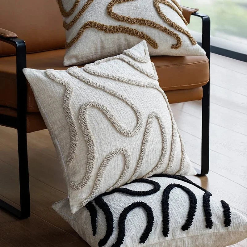 Coussins décoratifs aux motifs géométriques en beige et noir, posés sur un canapé moderne en cuir