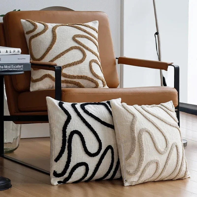 Coussins décoratifs aux motifs géométriques en beige et noir, posés sur un fauteuil moderne en cuir