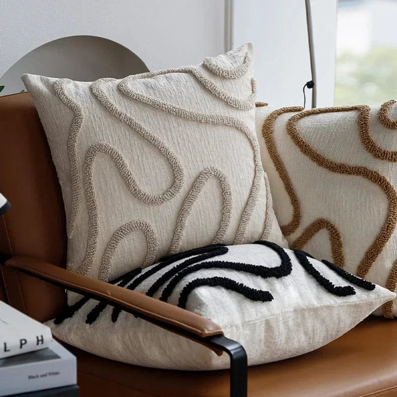 Coussins décoratifs aux motifs géométriques en beige et noir, posés sur un canapé en cuir moderne