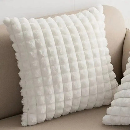 Coussin décoratif blanc en matière douce avec un motif texturé, posé sur un canapé beige