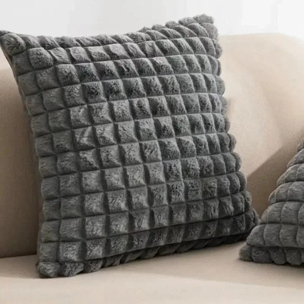 Coussin déco en velours gris, à motif carré, posé sur un canapé beige, ajoutant une touche moderne à la décoration