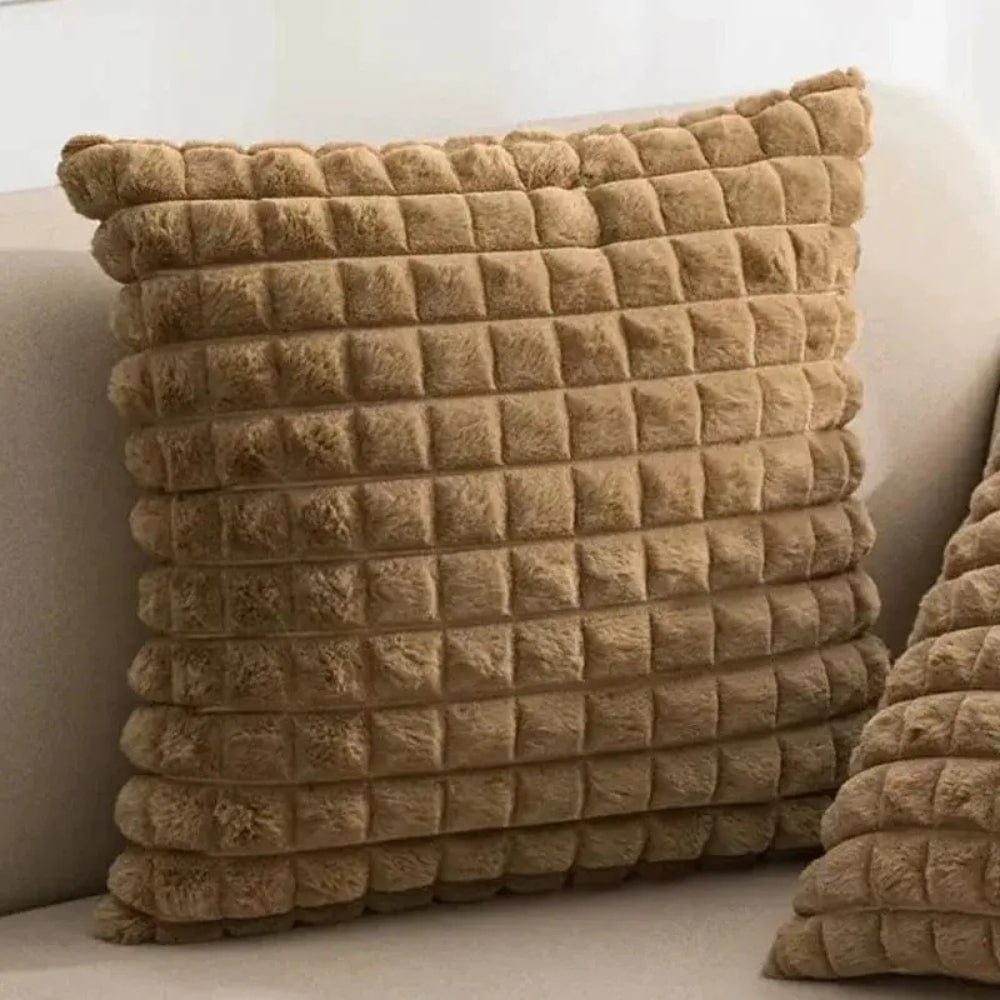 Coussin décoratif en velours beige à motifs carrés, posé sur un canapé moderne dans un salon élégant
