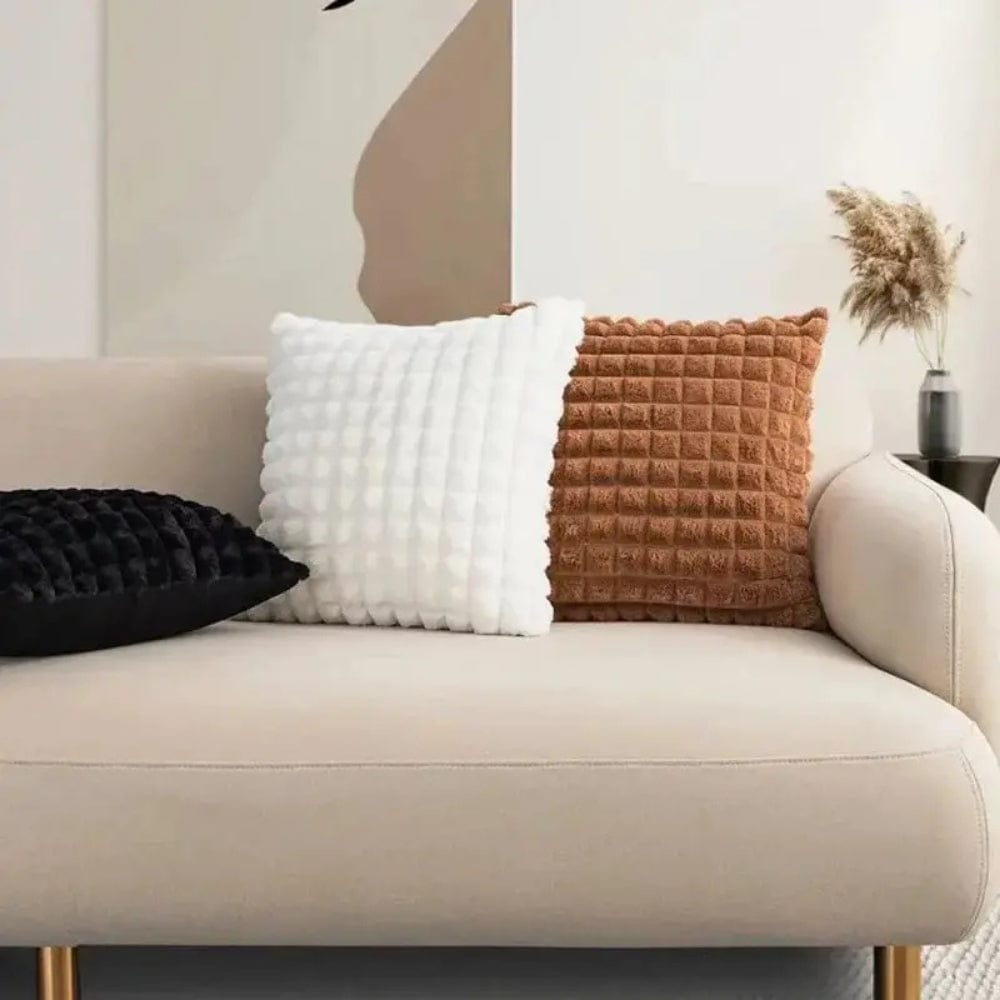 Trois coussins décoratifs aux textures variées, noir, blanc et brun, sur un canapé beige moderne