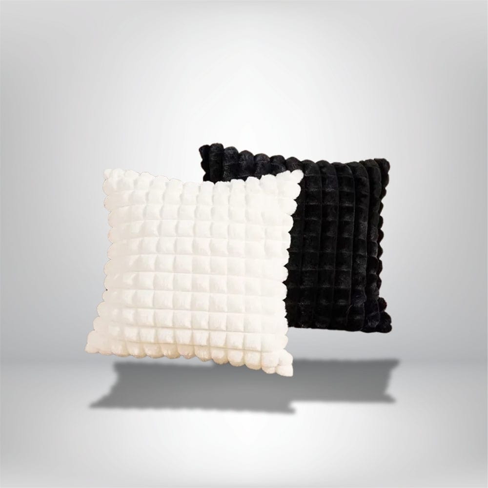 Deux coussins décoratifs, l'un blanc et l'autre noir, en velours texturé, posés sur un fond neutre