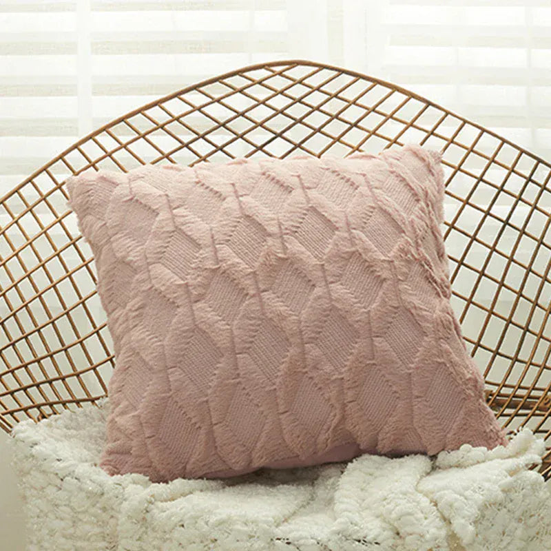 Coussin décoratif rose avec un motif texturé, posé sur un fauteuil en rotin dans un salon lumineux