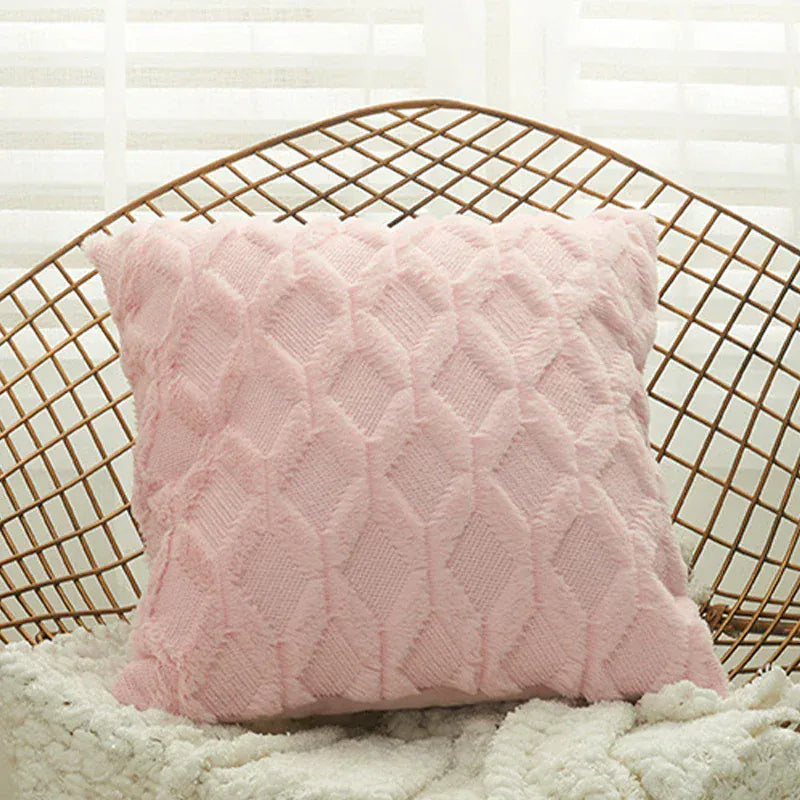 Coussin décoratif rose en matière douce avec motif en losanges, posé sur un fauteuil en osier