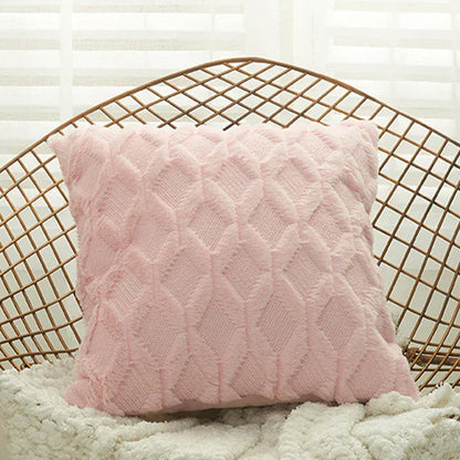 Coussin décoratif rose en matière douce avec motif en losanges, posé sur un fauteuil en osier