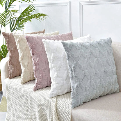 Quatre coussins décoratifs aux teintes douces, en matière texturée, posés sur un canapé avec un plaid