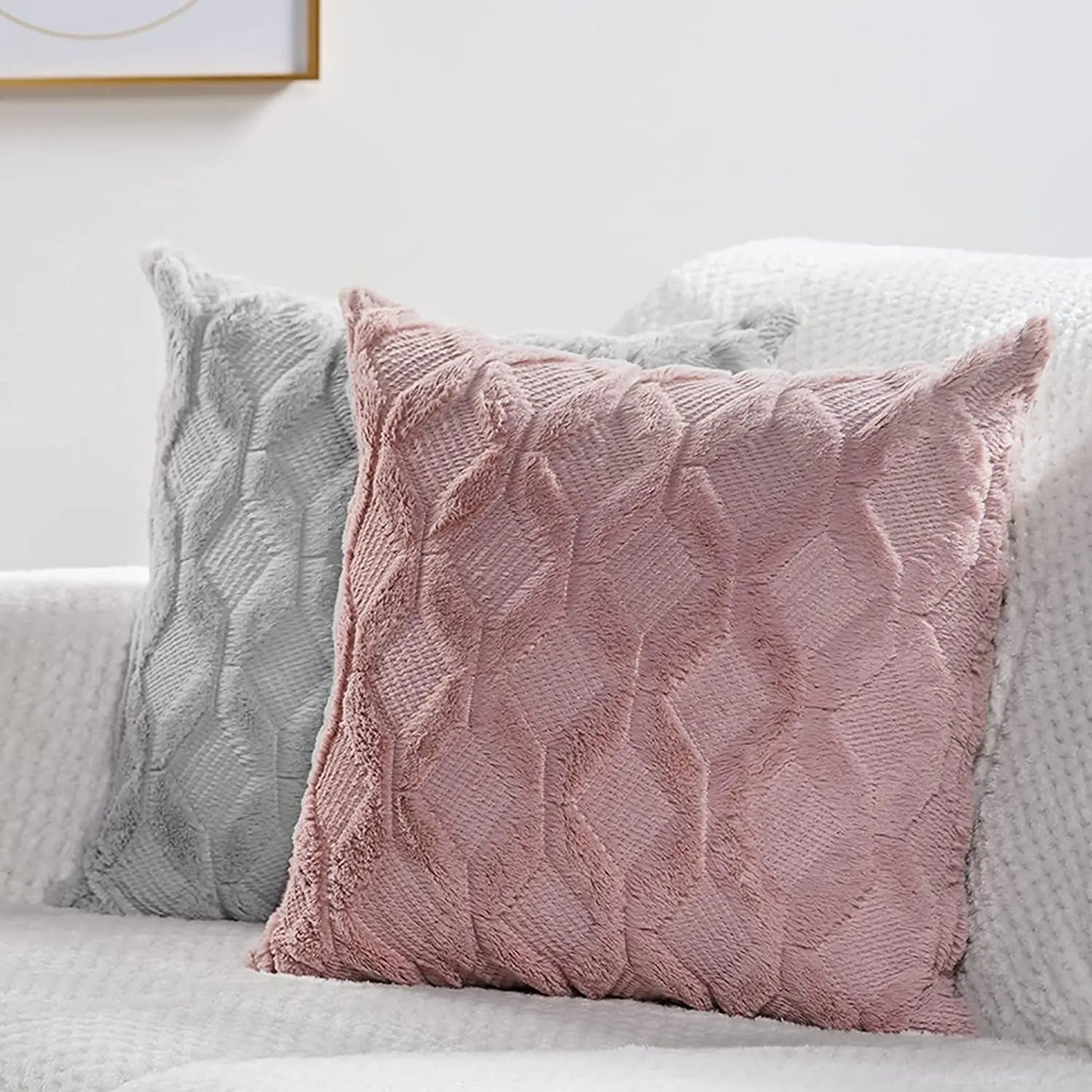 Coussins décoratifs en velours rose et gris avec motifs en relief, posés sur un canapé blanc