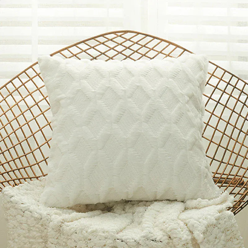 Coussin décoratif blanc en tissu doux avec un motif texturé, posé sur un fauteuil en rotin dans un salon lumineux