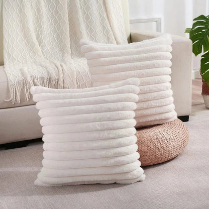 Deux coussins décoratifs en fausse fourrure blanche, posés sur un tapis dans un salon cosy