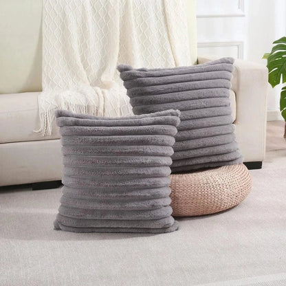 Deux coussins décoratifs en fausse fourrure grise, posés sur un tapis, à côté d'un canapé beige
