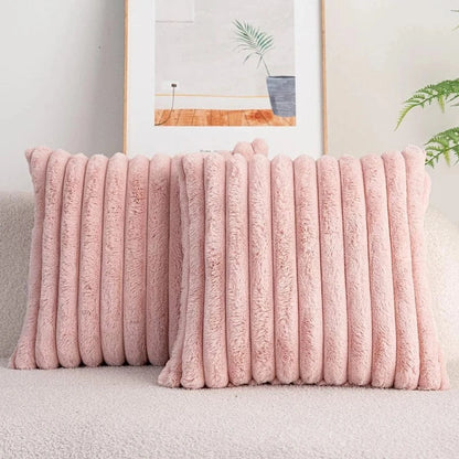 Deux coussins décoratifs en fausse fourrure rose, posés sur un canapé beige, ajoutent une touche cocooning