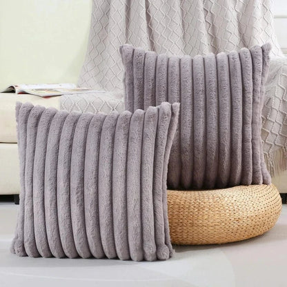 Coussins décoratifs en fausse fourrure douce, couleur gris, posés sur un pouf en osier dans un salon cocooning