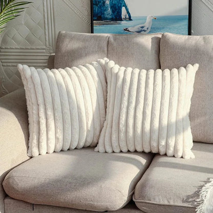 Deux coussins décoratifs en fausse fourrure blanche posés sur un canapé beige, créant une ambiance cocooning