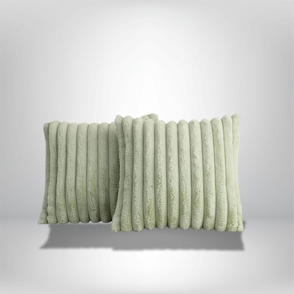 Deux coussins décoratifs en fausse fourrure douce de couleur vert pastel, posés sur une surface neutre