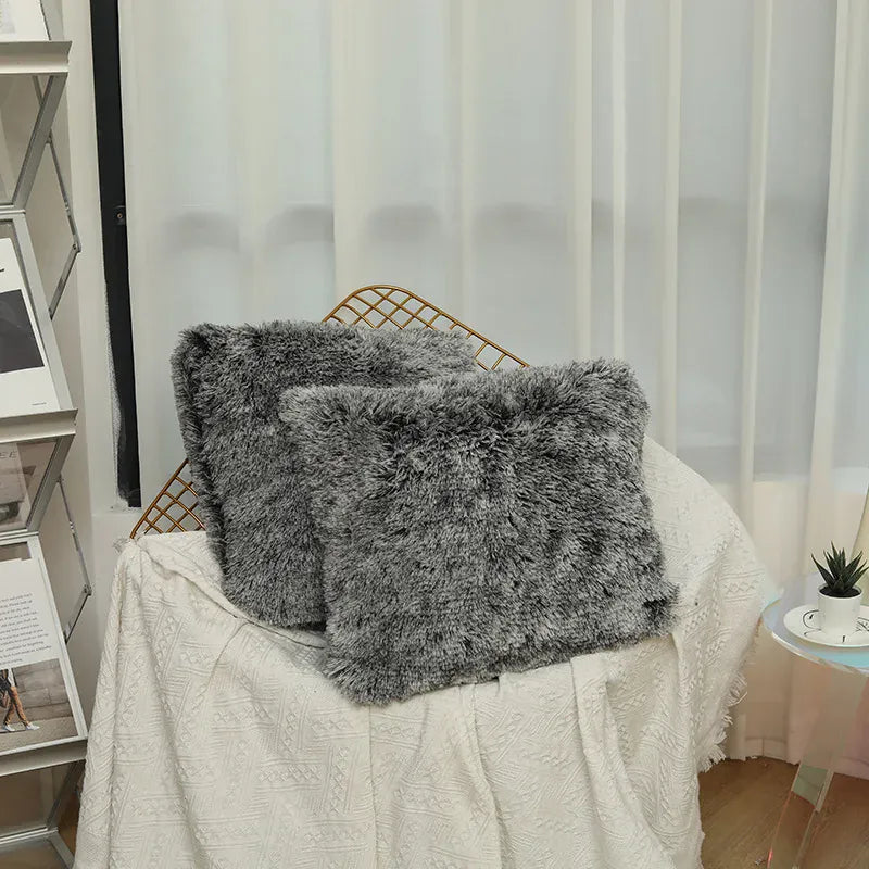 Deux coussins décoratifs en fausse fourrure grise posés sur un canapé recouvert d'un plaid blanc