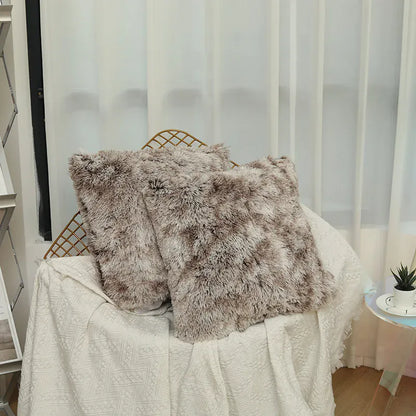 Deux coussins décoratifs en fausse fourrure beige posés sur un canapé recouvert d'un plaid blanc