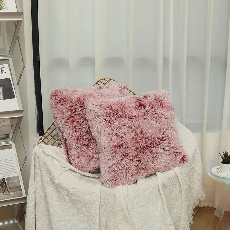 Deux coussins en fausse fourrure rose posés sur un canapé décoré d'un plaid blanc dans un salon lumineux