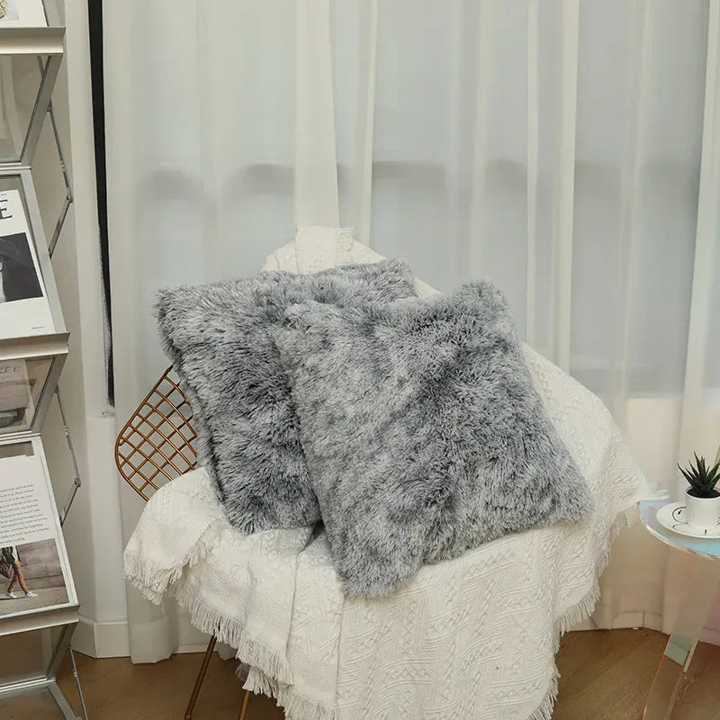 Deux coussins en fausse fourrure grise posés sur un fauteuil, décorant un coin de salon chaleureux