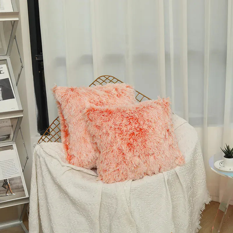 Deux coussins décoratifs en fausse fourrure rose, posés sur un canapé avec un plaid blanc