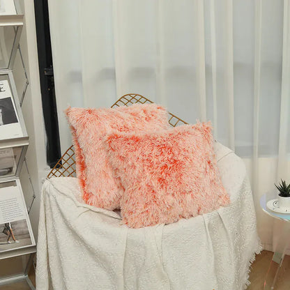 Deux coussins décoratifs en fausse fourrure rose, posés sur un canapé avec un plaid blanc