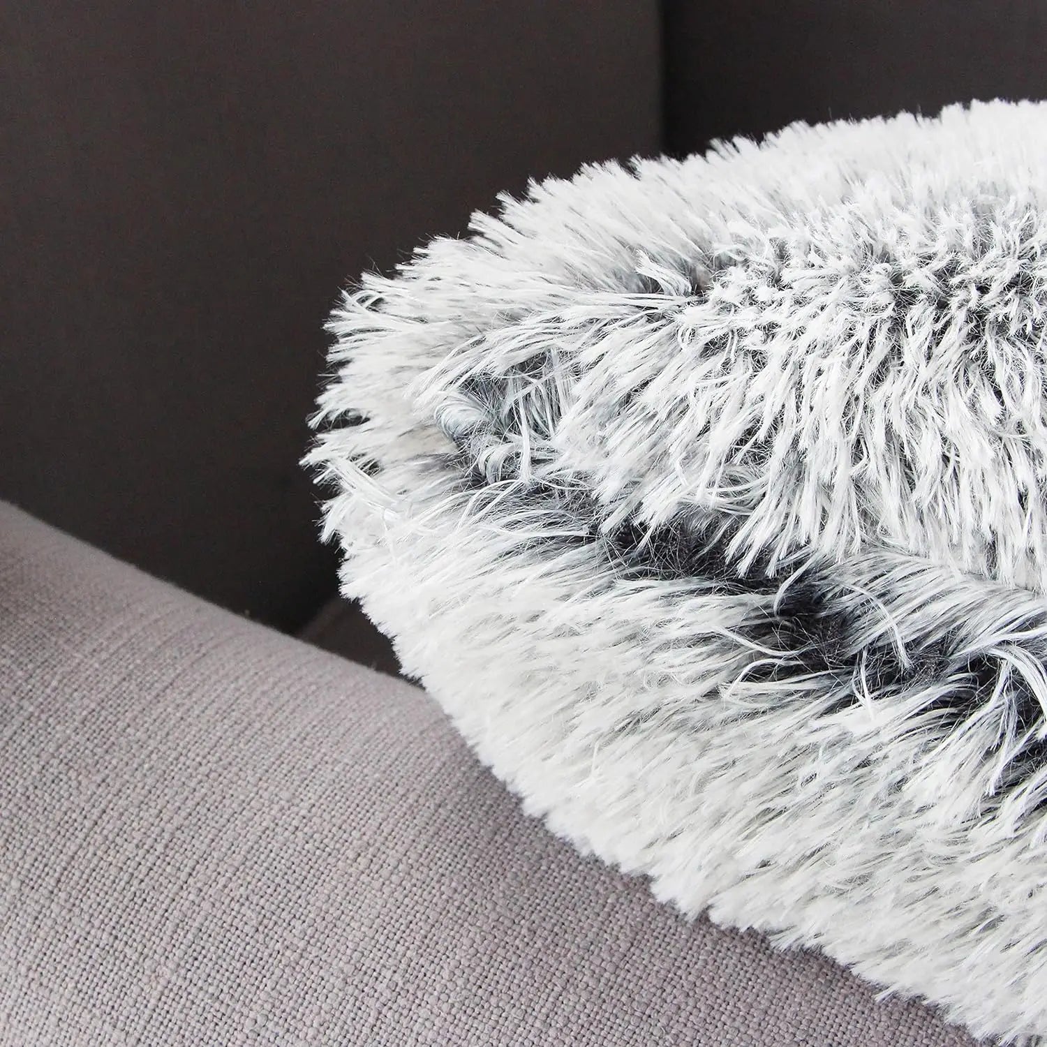 Coussin décoratif en fausse fourrure grise et blanche posé sur un canapé en tissu beige