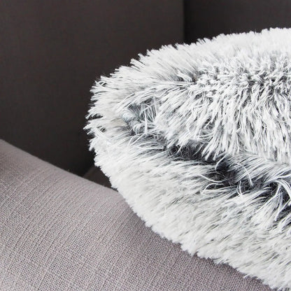 Coussin décoratif en fausse fourrure grise et blanche posé sur un canapé en tissu beige