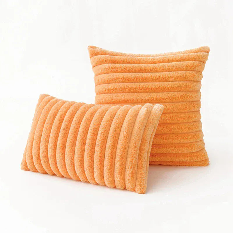 Coussins décoratifs en fourrure orange avec des motifs rayés, posés sur un fond blanc