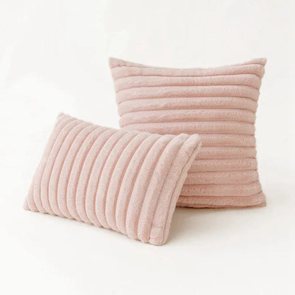 Coussins décoratifs en fourrure rose avec des motifs rayés, posés sur un fond neutre