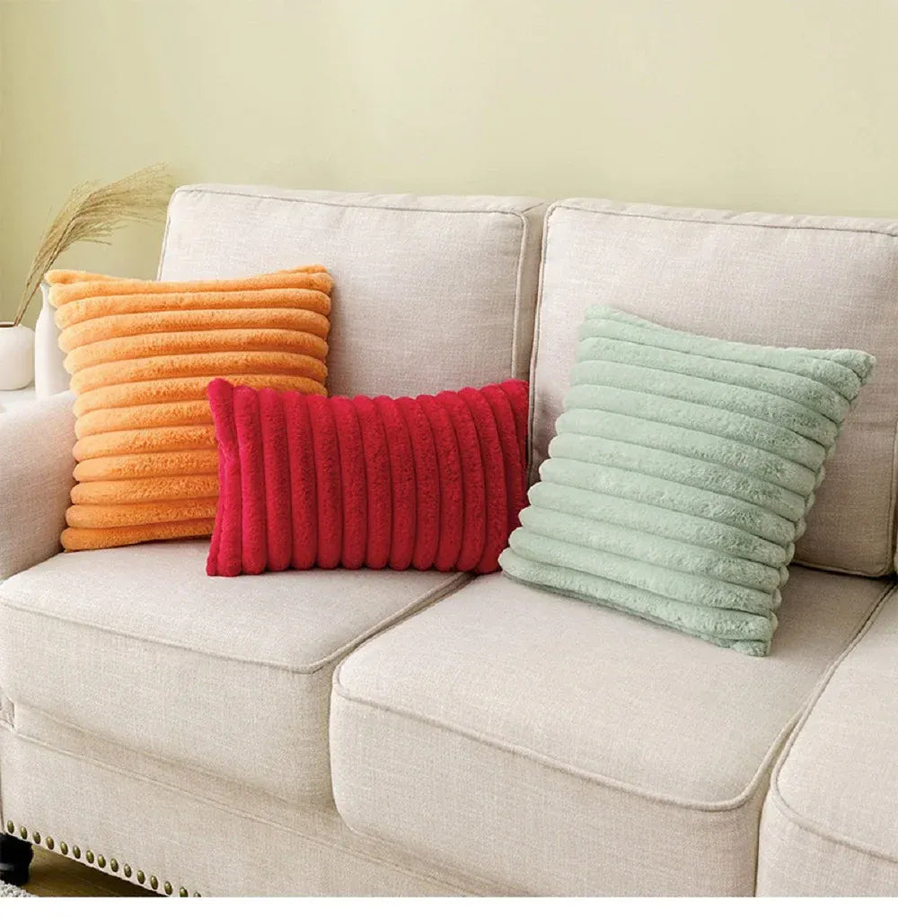 Trois coussins décoratifs en fourrure aux couleurs orange, rouge et vert sur un canapé beige