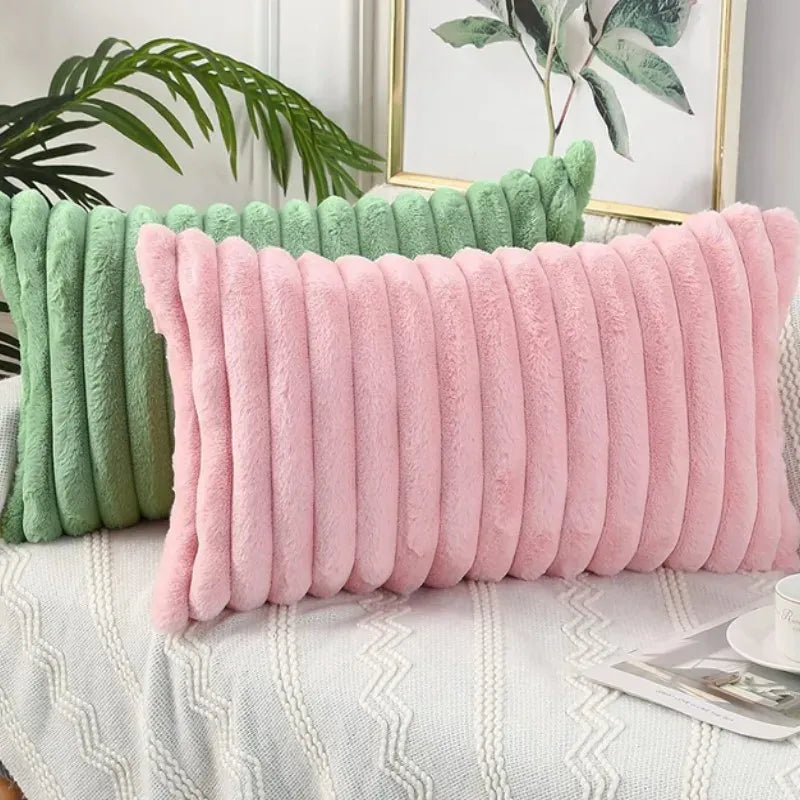 Coussins décoratifs en fourrure rose et vert, disposés sur un canapé avec un plaid en tricot