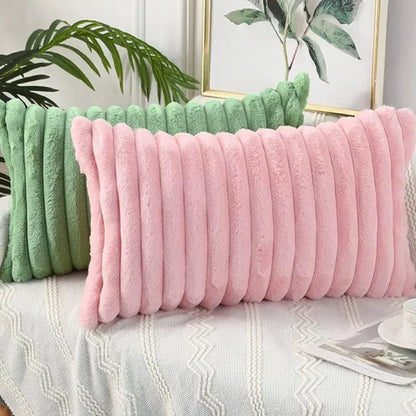 Coussins décoratifs en fourrure rose et vert, disposés sur un canapé avec un plaid en tricot