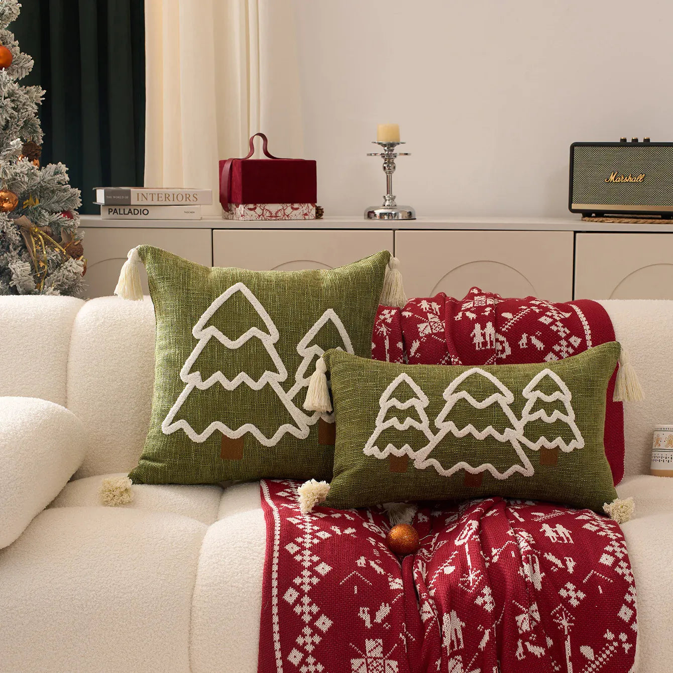 Coussins décoratifs en lin vert avec motifs d'arbres blancs, posés sur un canapé blanc avec un plaid rouge