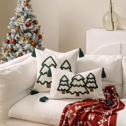 Coussins décoratifs en lin blanc avec motifs de sapins verts et pompons, posés sur un canapé clair