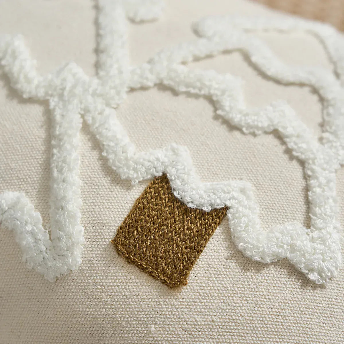 Housse de coussin en lin beige avec motifs en relief blancs et un détail en fil doré sur un canapé
