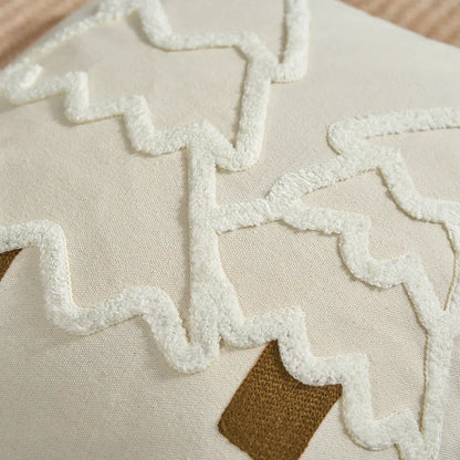 Housse de coussin en lin beige avec motifs en relief blancs et bruns, posée sur un canapé