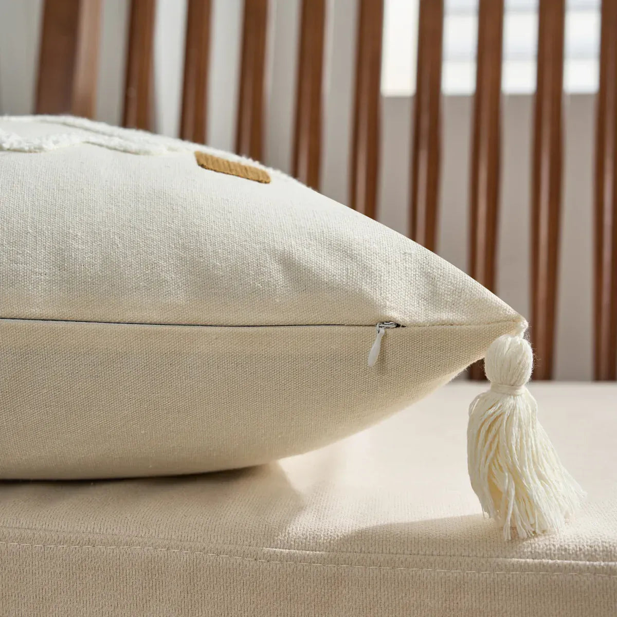 Housse de coussin en lin beige avec un pompon, posée sur un canapé clair en tissu