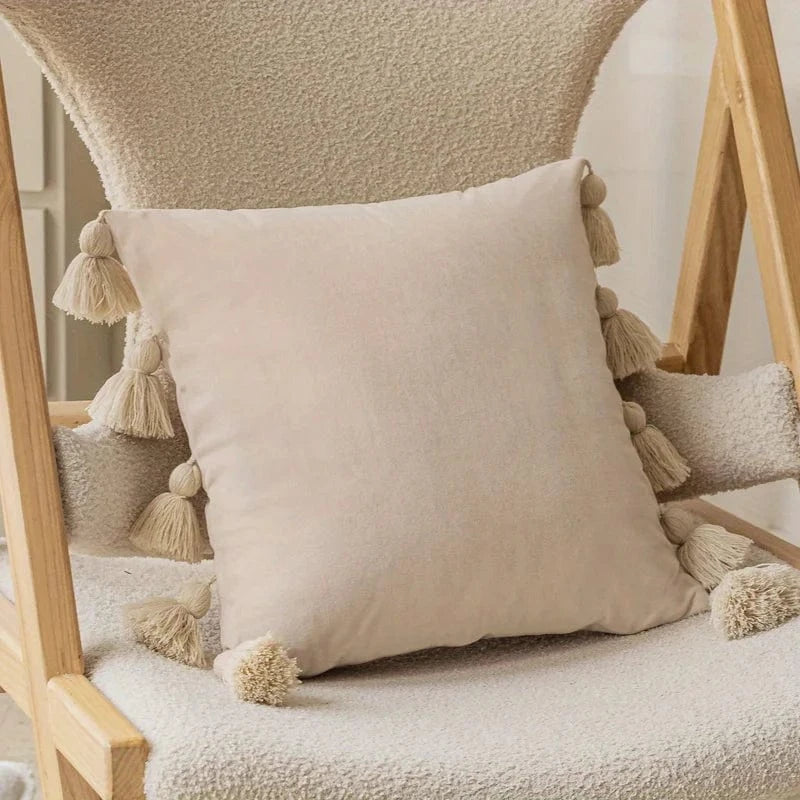 Coussin déco en velours beige avec pompons, posé sur une chaise en bois dans un salon moderne