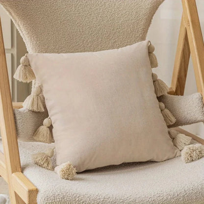 Coussin déco en velours beige avec pompons, posé sur une chaise en bois dans un salon moderne