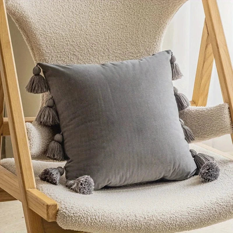 Coussin décoratif en velours gris avec pompons, posé sur une chaise en bois dans un salon moderne