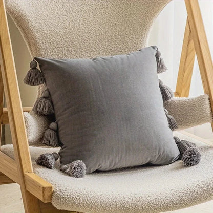 Coussin décoratif en velours gris avec pompons, posé sur une chaise en bois dans un salon moderne