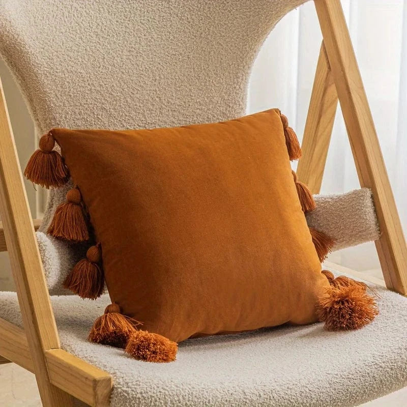 Coussin décoratif en velours orange avec pompons, posé sur une chaise en bois dans un salon moderne