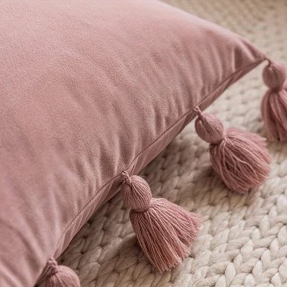 Housse de coussin en velours rose avec des pompons, posée sur un tapis tressé dans un salon chaleureux